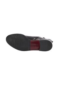 Presa di una scarpa in pelle nera con una finitura liscia, suola a tramatura distintiva per una presa aderente e una sezione rossa accentuata vicino al tallone.
