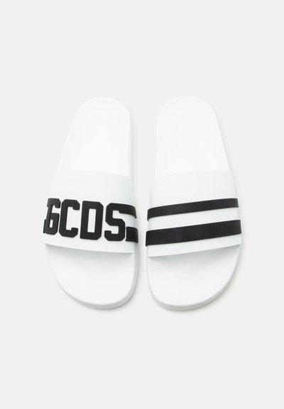 Sandales à enfiler blanches avec des lettres "GCDS" en relief noir sur la bride gauche et deux bandes noires sur la bride droite.