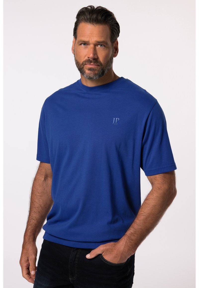 T-shirt blu a maniche corte in tessuto morbido con scollo rotondo e un logo discreto sul lato sinistro del petto. Indossato con jeans scuri.