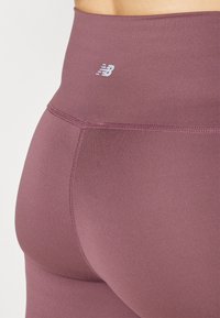 Leggings taille haute dans une couleur mauve douce, fabriqués à partir d'un tissu lisse et extensible, avec des coutures tonales et un petit logo.