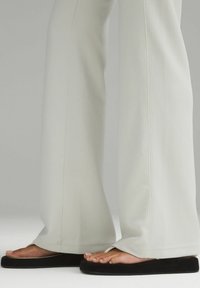 Vaaleanharmaat ribbikuvioiset leveät housut, joissa on joustava vyötärö, yhdistetty mustiin litteisiin sandaaleihin, joissa on valkoinen nauha.