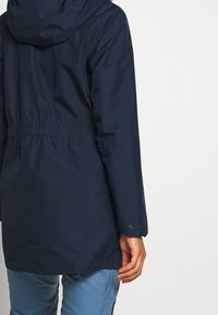Veste imperméable marine avec capuche, taille cintrée et manches longues. Comprend des boutons-pression aux poignets et une texture lisse et durable.