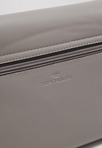 Szara torebka kopertowa z syntetycznej skóry o gładkiej fakturze, z zamkiem błyskawicznym i wytłoczonym napisem "TOM TAILOR" nad zamkiem.