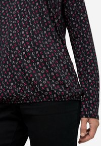 Langarmshirt in Schwarz mit einem wiederholten Muster aus pinkem und weißem Text. Weicher Stoff mit leichtem Stretch und rundem Ausschnitt.