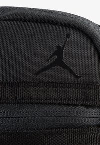 Czarny plecak z materiału o gładkiej fakturze, z wyraźnym czarnym logo Jumpman oraz starannie wykonanym przeszyciem. Minimalistyczny design.