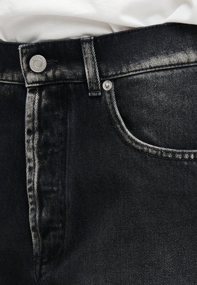 Κοντινό πλάνο στη μέση μαύρου τζιν με ασημένιο κουμπί και λευκό ύφασμα που είναι βιδωμένο στη μέση.