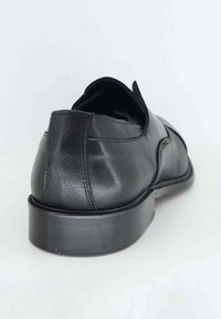 Scarpa in pelle nera con superficie liscia, forma arrotondata, tacco a blocco e dettagli di cucitura discreti sul retro.