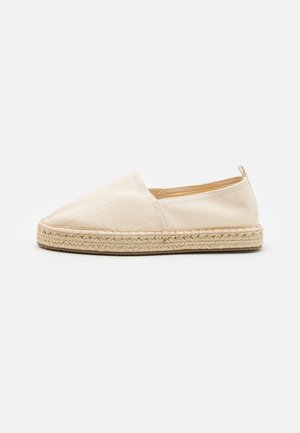 Beige espadrille schoen met een canvas bovenwerk en een gevlochten jute zool. Heeft een ronde teen en een instapontwerp. Soepele textuur met minimale details.