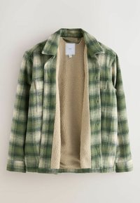 Zaļš šaķets ar beige krāsas vilnas oderi, ar apkakli, garām piedurknēm un pogu aizdari. Audumam ir mīksta, struktūra.