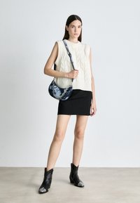 Pull sans manches en tricot crème avec motif torsadé, associé à une mini-jupe noire. Comprend un sac à main bleu tie-dye avec bandoulière chaîne et des bottines noires.