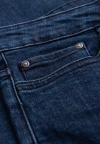 Tissu en denim bleu foncé avec un gros plan d'une petite poche avant, présentant un bouton argenté et des détails cousus le long des bords.
