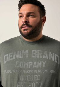 Olivgrüner Baumwollpullover mit großen, verblassten weißen Text, der "DENIM BRAND COMPANY" auf der Vorderseite zeigt, und einem gerippten Halsabschluss.