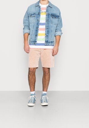 Spijkerjasje in lichtblauw, gestreept T-shirt met pasteltinten, roze corduroy korte broek en blauwe hoge sneakers.
