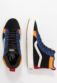 Hoge sneakers in zwart, blauw, oranje en rode suède en leer. Voorzien van een witte zijkantstreep, zwarte veters en een bruine rubberen zool.