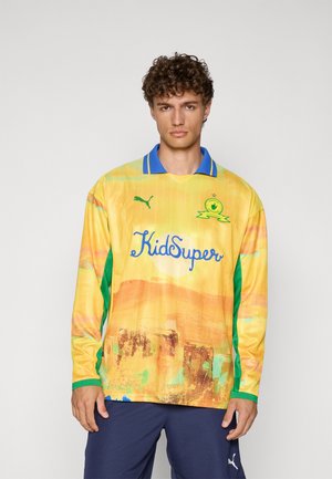 Maglia da calcio a maniche lunghe gialla con dettagli verdi, colletto blu, design grafico e marchio "KidSuper" sul davanti. Realizzata in tessuto leggero.