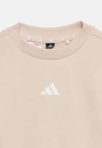 Μπεζ φούτερ με στρογγυλή λαιμόκοψη και ριμπ ύφανση στο γιακά, με μικρό λευκό λογότυπο Adidas στο κέντρο του στήθους.