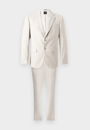 Costume pour homme deux pièces beige clair avec col cranté, veste à deux boutons, poches à rabat et pantalon assorti, présenté sur un fond uni.
