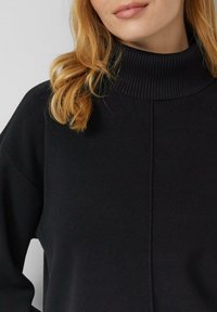 Schwarzer Rollkragenpullover mit geripptem Kragen, entspannter Passform und weicher Textur. Einfaches Design mit minimalen Nähten und Details.