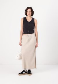 Top senza maniche nero a righe con bottoni, abbinato a una gonna maxi beige con vita regolabile, sneakers nere e una piccola borsa bianca.