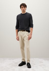 Maglione lavorato a maglia grigio scuro, pantaloni beige, scarpe in pelle nere. L'outfit presenta un collo rotondo e una cintura marrone con una fibbia in tono oro.