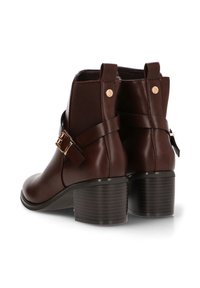 Botas de tobillo marrones de cuero con suela texturizada, correa decorativa y hebilla, y paneles laterales elásticos para mayor flexibilidad.