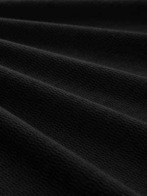 Melna teksturēta auduma ar ribotu rakstu, kas izceļ vairākas locījums un viļņus, uzsverot matētu virsmu un izturīgu izskatu.