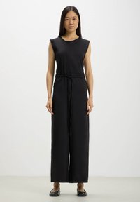 Jumpsuit nero senza maniche con vita stretta, gambe ampie e texture liscia. Presenta un collo rotondo e un design minimalista.