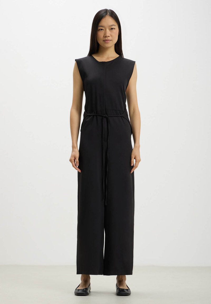 Jumpsuit nero senza maniche con vita stretta, gambe ampie e texture liscia. Presenta un collo rotondo e un design minimalista.