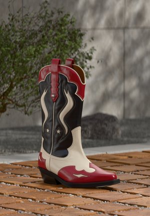Botte de cowboy rouge, noire et blanche avec des motifs d'étoile et de flammes, posée sur une surface en briques avec un fond flou de plante et de mur.
