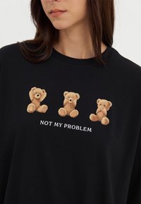 Black cotton t-shirt featuring three plush teddy bear graphics and the text "NOT MY PROBLEM" in white. Round neckline, relaxed fit.