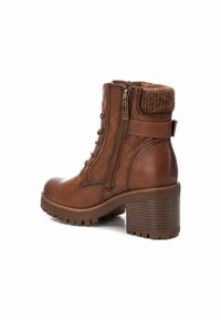 Botín marrón hasta el tobillo con un acabado texturizado, diseño acolchado, cremallera lateral y un tacón grueso. Cuenta con una suela acanalada y un detalle suave en el puño.