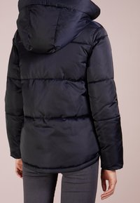 Marinblå puffjacka med huva, med kviltade sektioner, mjuk textur och elastiska ärmslut. Designad för värme och täckning.