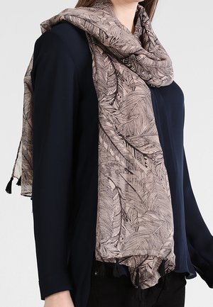 Femme portant une écharpe mauve clair avec un motif détaillé de plumes sur un chemisier à manches longues foncé, les extrémités de l'écharpe pendent avec des franges.