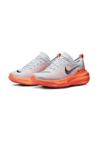 Pár fehér és narancssárga Nike futócipő fekete swoosh logókkal és "Invincible Run" felirattal az orrán.