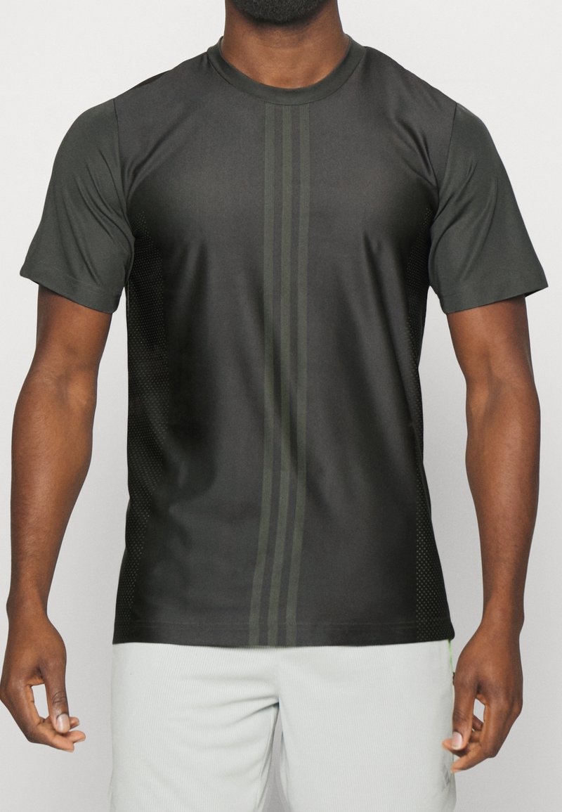 Camiseta atlética negra de manga corta, con rayas verticales verdes y un panel lateral texturizado. Hecha de tela que absorbe la humedad.