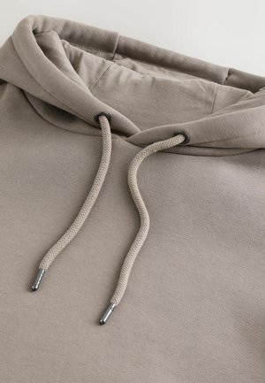 Beige hættetrøje med blød tekstur, der har en hætte med snøre og metalender, samt en afslappet pasform, lavet af en bomuldsblanding.
