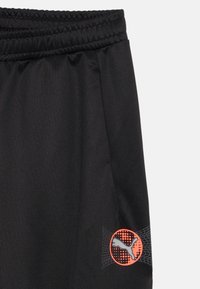 Pantalones cortos deportivos negros con cintura elástica, con un logo de Puma en naranja y detalles de malla gris en el lado inferior. Textura suave.