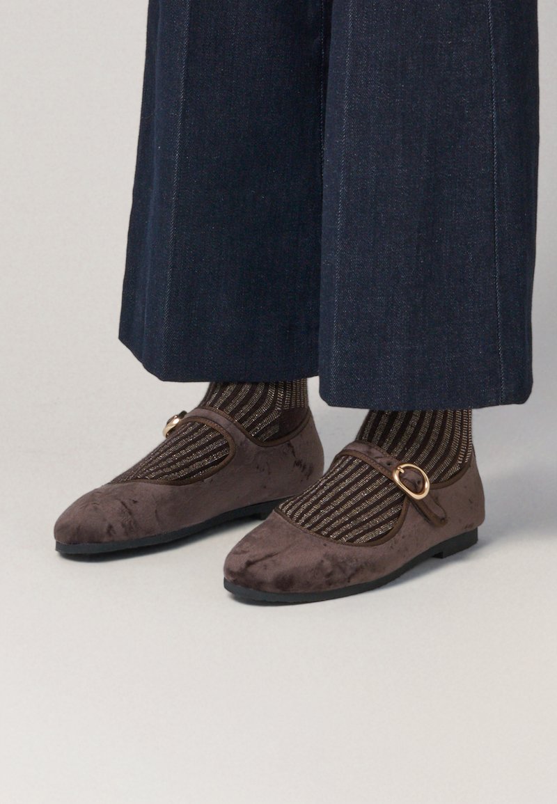 Scarpe Mary Jane in suede marrone con punta rotonda, suola piatta e una fibbia decorativa dorata. Abbinato a calzini rigati marrone scuro.