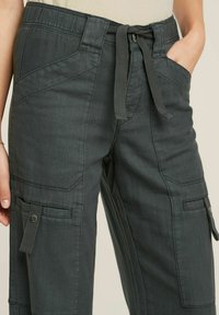 Pantaloni cargo grigio scuro realizzati in un tessuto morbido e texture. Le caratteristiche includono una vita con cordoncino, tasche laterali e dettagli di cucitura frontale.