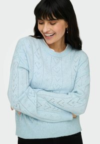 Pull tricoté bleu clair avec un motif géométrique incluant des formes de cœur et des détails en maille ajourée. Ourlet et poignets côtelés. Manches longues.