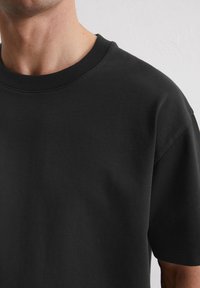 Zwarte katoenen T-shirt met een ronde hals en korte mouwen, met een gladde textuur en een minimalistisch ontwerp zonder patronen of accenten.