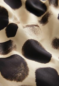 Kangas, jossa on sileä, beige kangas, johon on koristeltu epäsäännöllisillä mustilla ja tummanruskeilla pilkuilla, luoden rohkean eläinkuosin.