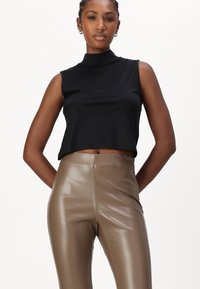 Top nero senza maniche con collo alto e design corto, abbinato a leggings aderenti lucidi di colore marrone chiaro a vita alta. Texture complessivamente liscia.