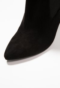 Černé semišové kotníkové boty s špičatou špičkou a hladkým povrchem. Mají elegantní design a elastické boční akcenty pro snadné obouvání.