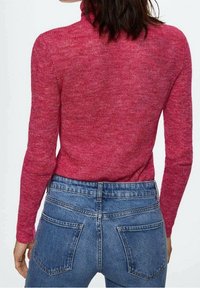 Pull-over ajusté en maille magenta texturée avec un col montant, associé à un jean bleu taille mi-haute avec poches arrière.