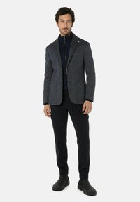 Blazer in marineblauwe geruite patroon met een getailleerd ontwerp, gecombineerd met een donkerblauwe gebreide jas, zwarte broek en donkere schoenen.