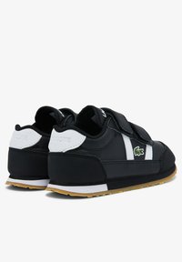 Černé tenisky s suchým zipem, bílými akcenty a zeleným krokodýlím logem. Gumená podrážka s texturovaným povrchem pro lepší přilnavost.