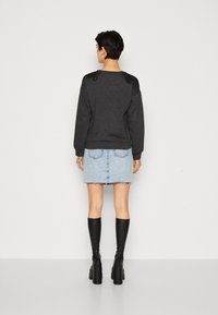 Sweatshirt noir avec des accents texturés sur les épaules, associé à une mini-jupe en denim bleu clair et des bottes noires en cuir jusqu'aux genoux.