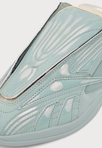 Gros plan d’un bout de sneaker bleu clair brillant avec des motifs de couture blancs et argentés complexes et des détails de semelle texturés.