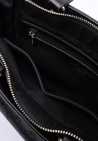 Interno di una borsa a tracolla nera in pelle, con una cerniera dorata, una tasca con cerniera e un compartimento aperto, che mostra l'imbottitura in tessuto e i dettagli delle cuciture.
